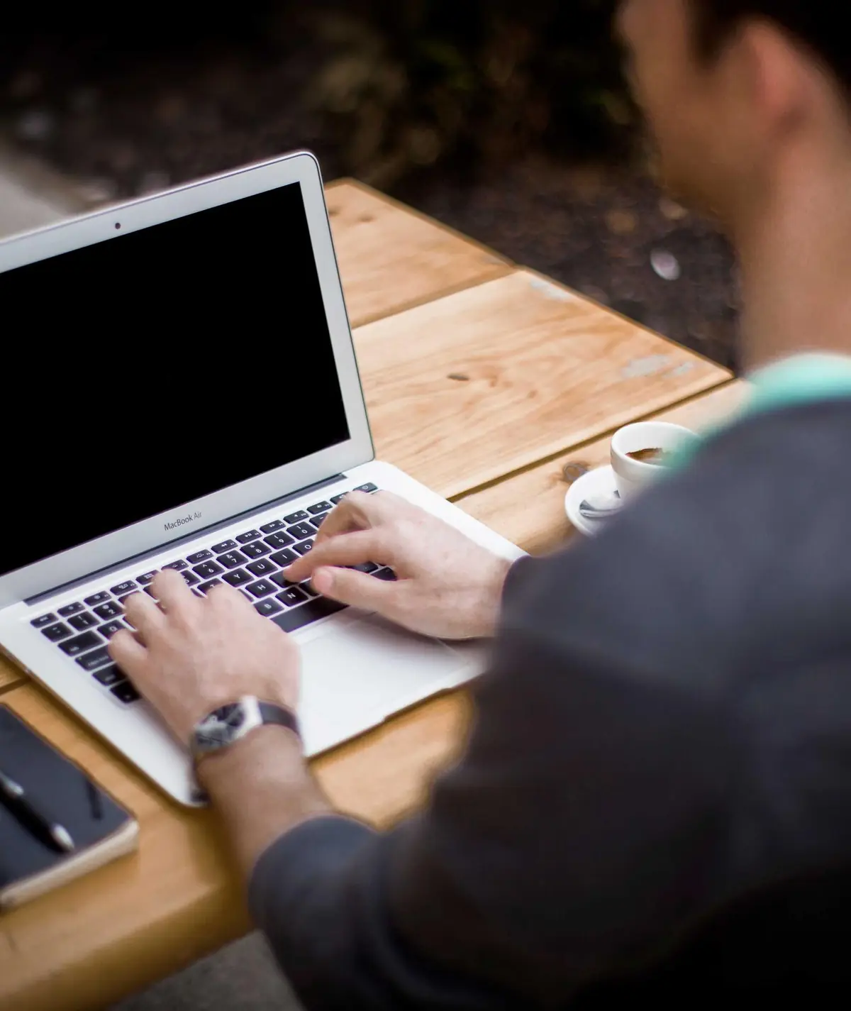 A developer typing on a laptop at a wooden desk