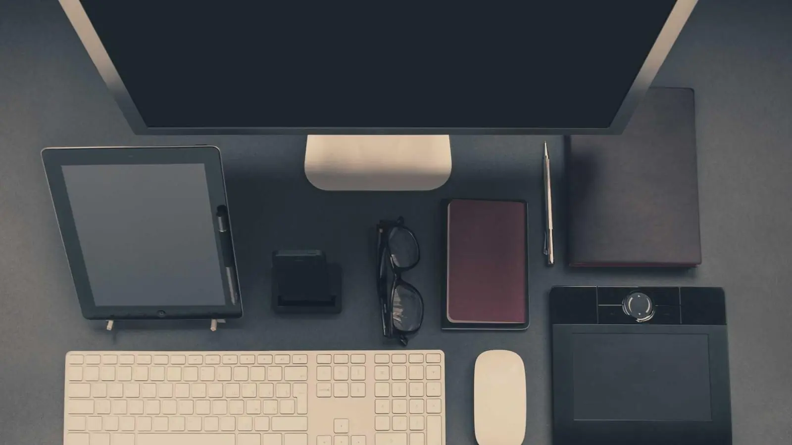 A designer's desk from above with a monitor, keyboard, tablet and drawing pad