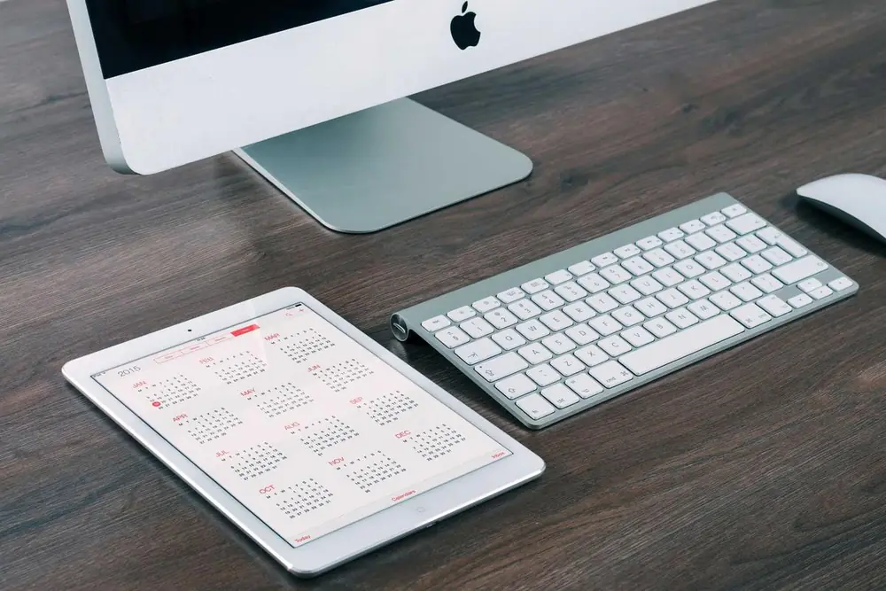 A desktop computer, wireless keyboard and tablet on a dark wooden desk
